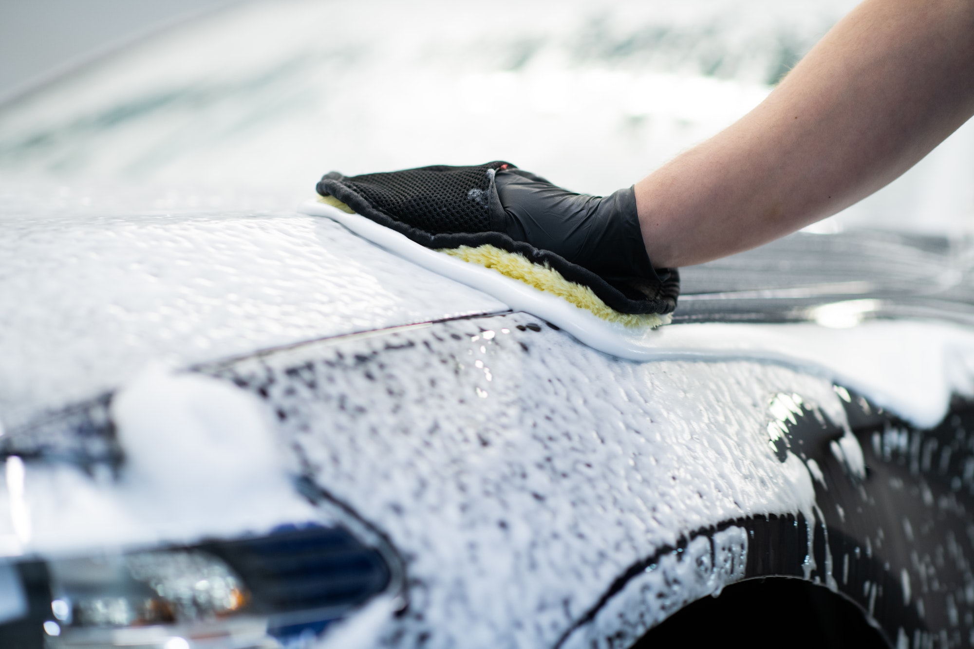 Man washing a soapy black car in a cleaning and detailing service