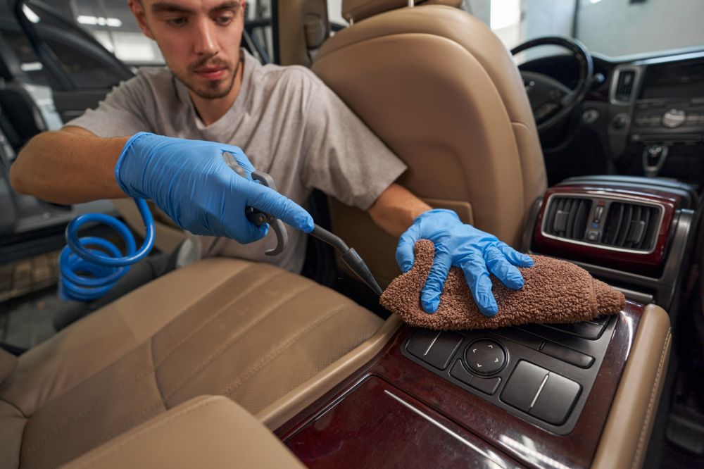 Spezialist für Autoaufbereitung in Cloppenburg reinigt sorgfältig die Ledersitze eines Autos mit einem Dampfreiniger und einem Mikrofasertuch.