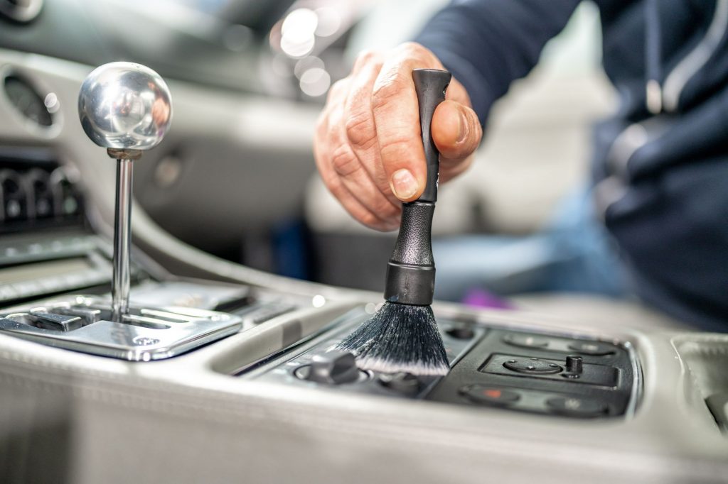 Eine Person reinigt sorgfältig den Innenraum eines Fahrzeugs mit einem Detailpinsel als Teil der Autoaufbereitung in Vechta.
