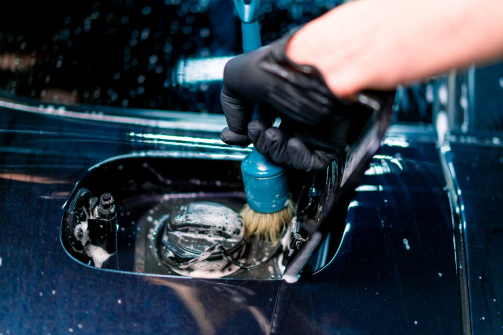 Professionelle Fahrzeugaufbereitung Bramsche - Nahaufnahme eines Technikers, der den Tankdeckel eines Autos gründlich mit einer Bürste reinigt.